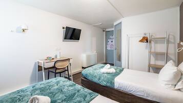 A small hotel room with two beds, a desk, a chair, a TV, and a door leading to a bathroom.