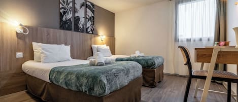A hotel room with a large bed, two bedside tables, a desk with a chair, and artwork on the wall.