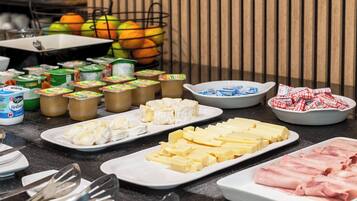 Una mesa de buffet con varios quesos, mantequilla y jamón.