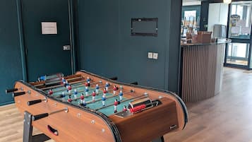 A foosball table in a room with a dark teal wall, wooden flooring, and pendant lighting.