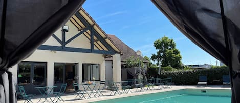 Zona de piscina con un área de estar techada y un edificio con techo de tejas.