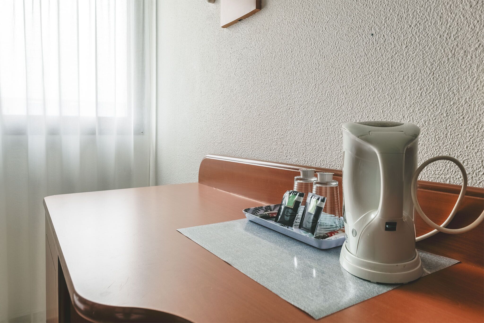 Une table avec une bouilloire électrique blanche, un plateau avec des bouteilles et un tapis.