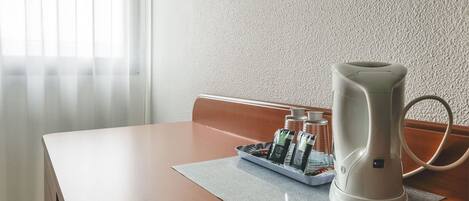 A table with a white electric kettle, a tray with bottles, and a mat.
