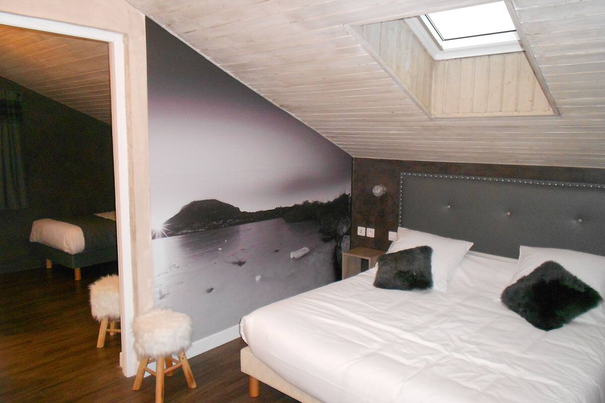 A bedroom with a bed, a nightstand, a stool, a wall mural, and a skylight.