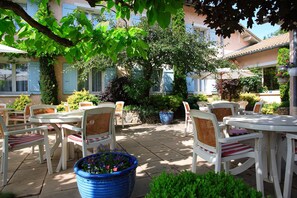 Une terrasse extérieure avec des tables et des chaises blanches, entourée d’une végétation luxuriante et de plantes en pot.