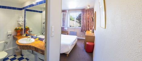 Una habitación de hotel con baño, cama, escritorio y ventana.