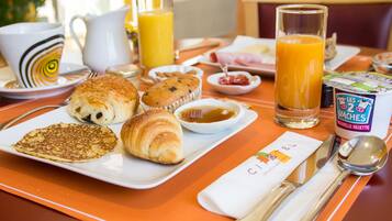 A breakfast tray with croissants, muffins, pancakes, and a glass of orange juice.