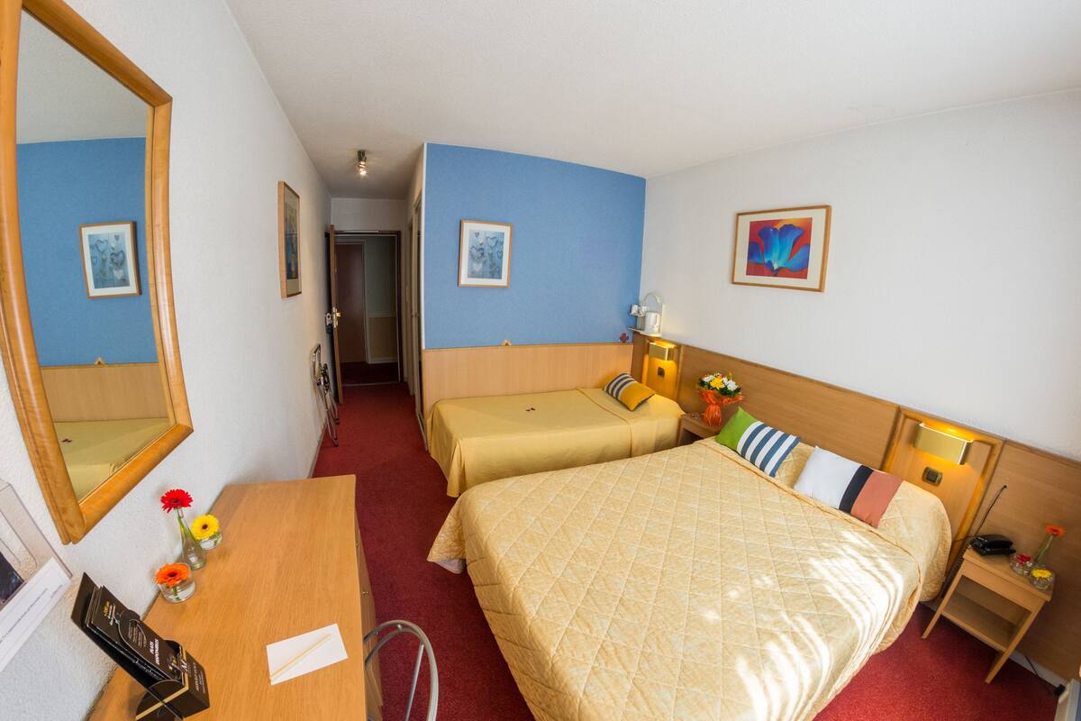 A hotel room with two beds, a desk, a chair, a mirror, and a nightstand with a lamp.