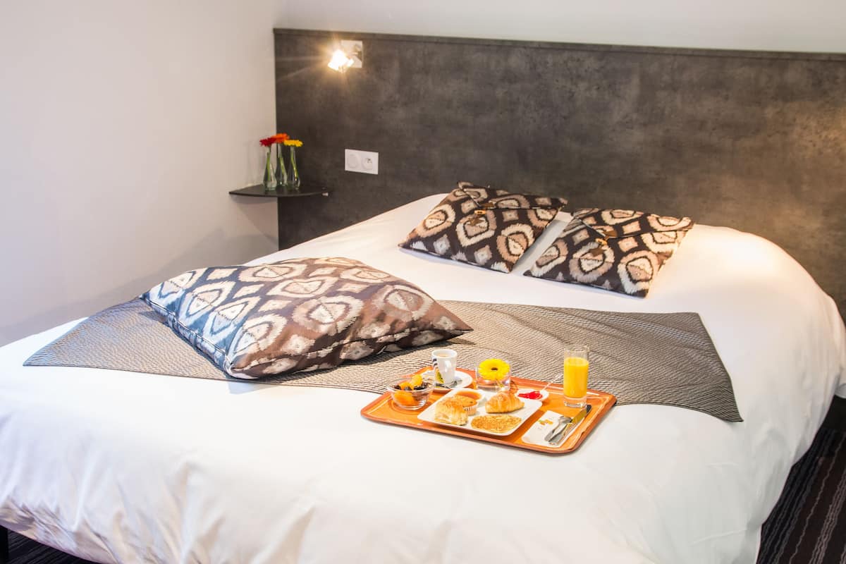 A neatly made bed with patterned pillows, a tray with breakfast items, and a vase with flowers on a bedside table.