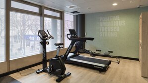Une salle de sport équipée de deux appareils d’exercice, dotée de grandes fenêtres, de citations motivantes affichées sur les murs et d’un plancher en bois.