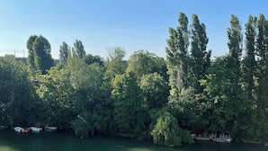 Une rivière bordée de bateaux amarrés sur la rive gauche, entourée d’une végétation dense et sous un ciel dégagé.