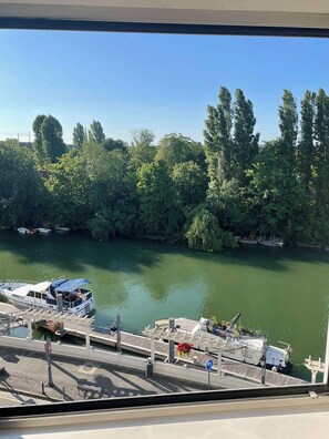 Ein Fluss mit vor Anker liegenden Booten auf der linken Seite, umgeben von dichtem Baumbestand und blauem Himmel.