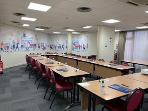 Ein Konferenzraum mit langen Tischen, roten Stühlen, Namensschildern und einem Feuerlöscher.
