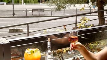 An outdoor dining area with a table set for two, featuring a drink, a bottle, a plate of food, and a selection of meats.