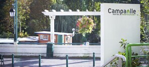 Une enseigne pour l’hôtel-restaurant Campanile, avec une pergola blanche et des fleurs suspendues en arrière-plan.