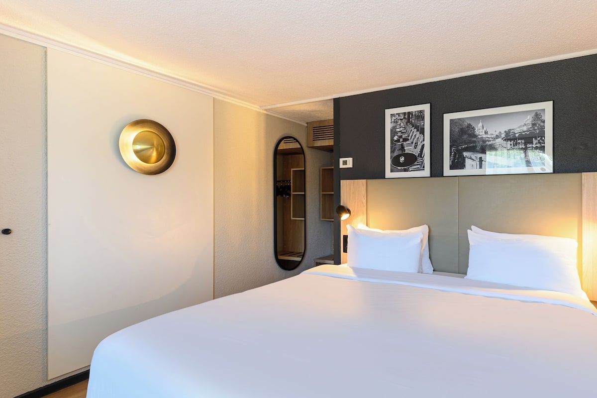 A hotel room with a large bed, two bedside lamps, a mirror, and two framed pictures on the wall.