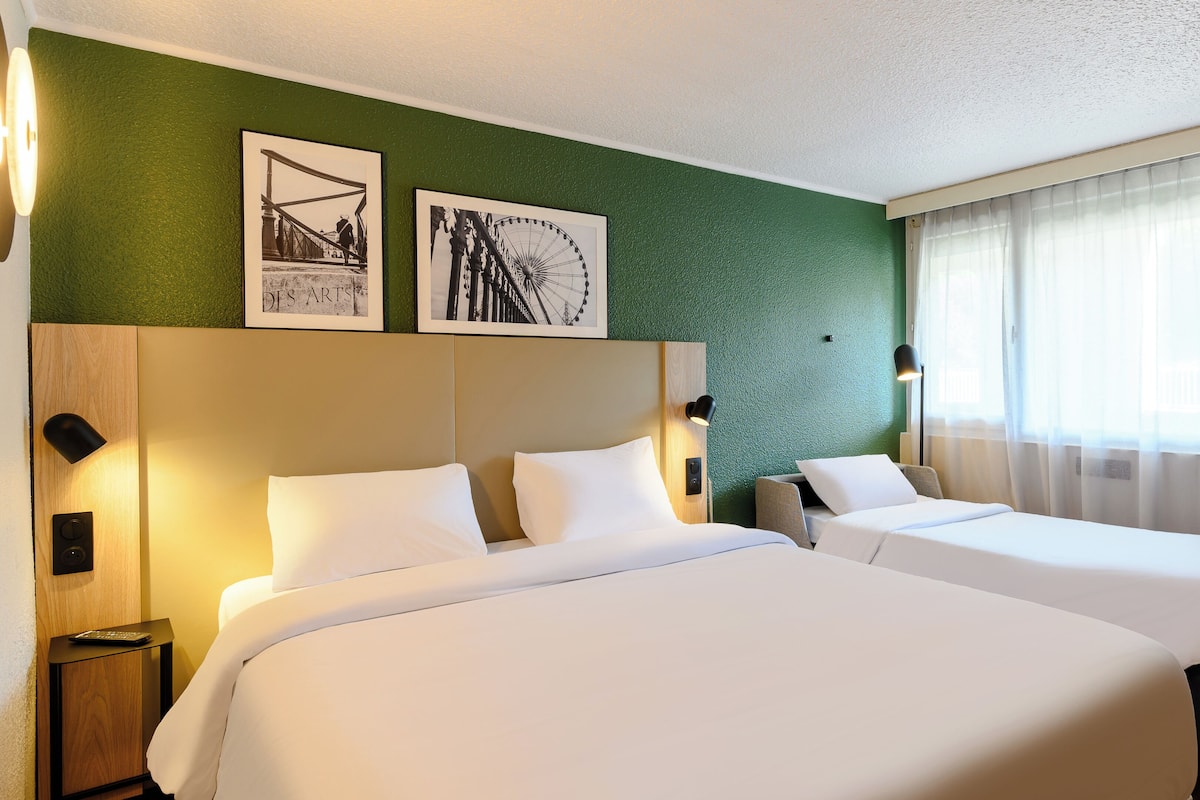 A hotel room with two beds, a green textured wall, and two framed pictures.