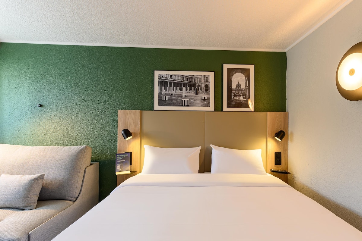 A hotel room with a bed, two pillows, a green wall, and two framed pictures.