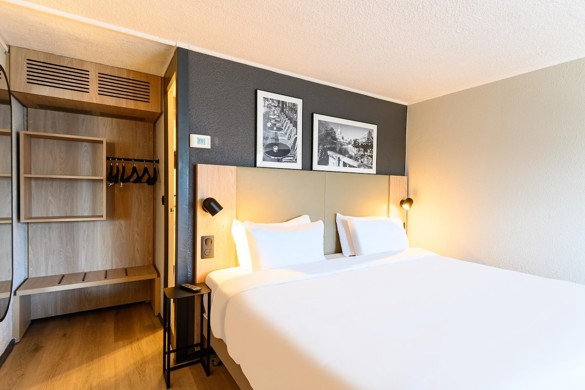 A hotel room with a bed, a wardrobe, and two framed pictures on the wall.