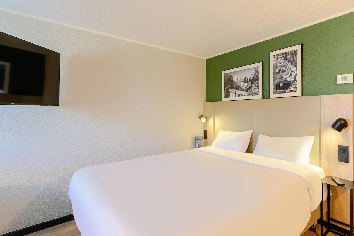 A hotel room with a large bed, a wardrobe, a coat rack, and two framed pictures on the wall.