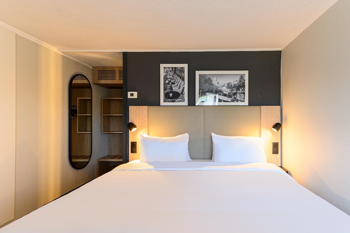 A hotel room with a large bed, two bedside lamps, a mirror, and two framed pictures on the wall.