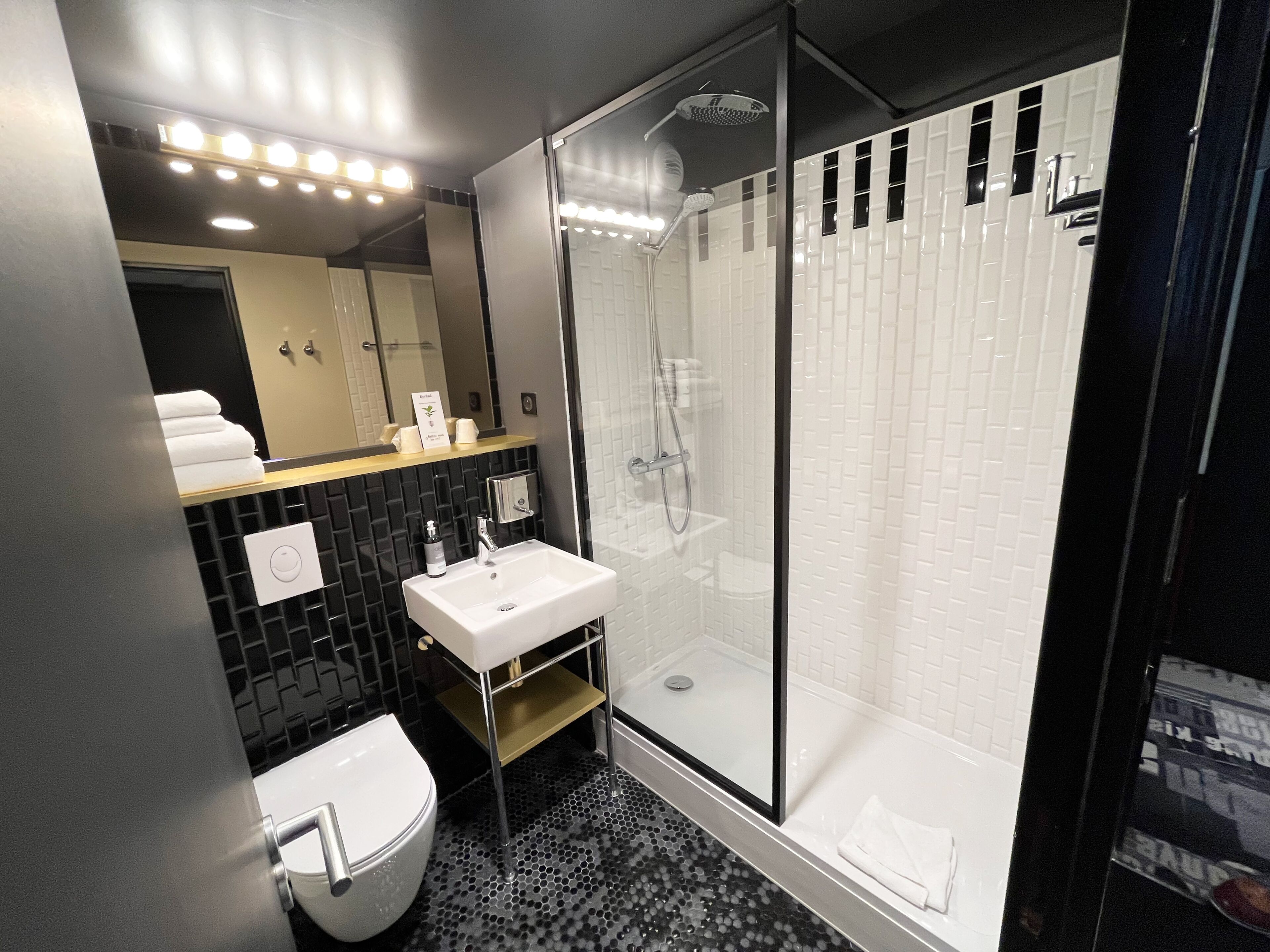 A modern bathroom with a glass-enclosed shower, a white sink, and a black tiled backsplash.