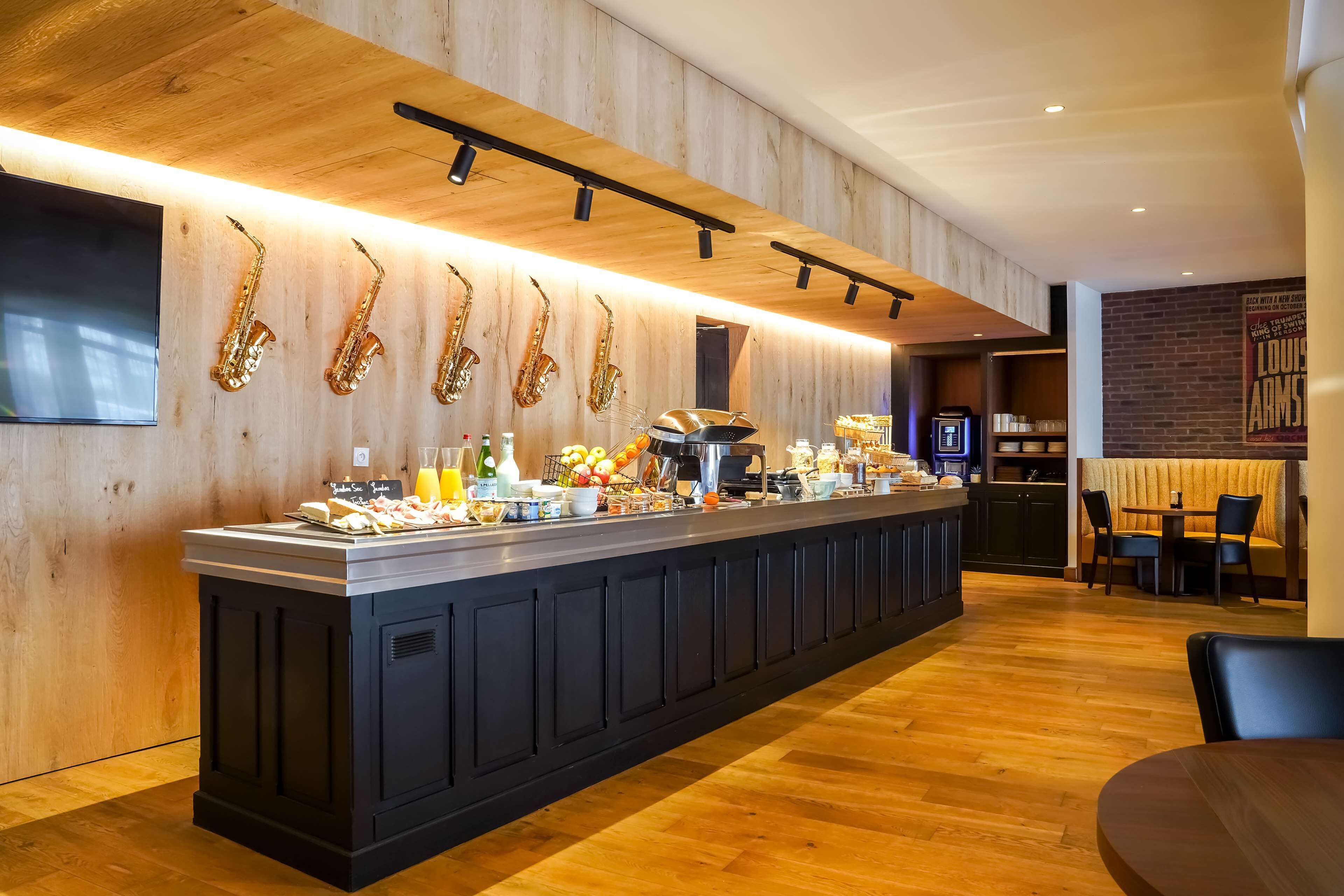 Bar de bufé con diversas opciones de comida y bebidas, una máquina de café y saxofones en la pared.