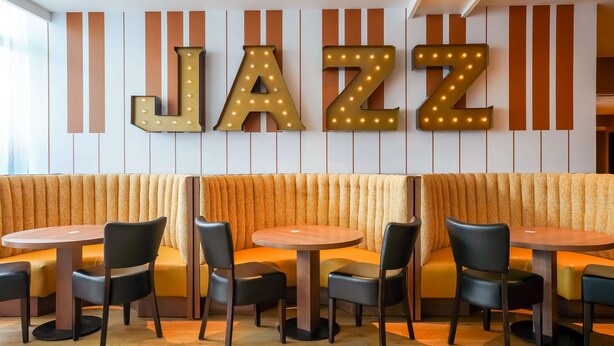 A jazz-themed restaurant interior with a large illuminated 'JAZZ' sign, cushioned seating, and round tables. - Hotel Kyriad Créteil/Bonneuil-sur-Marne (Bonneuil-sur-Marne)