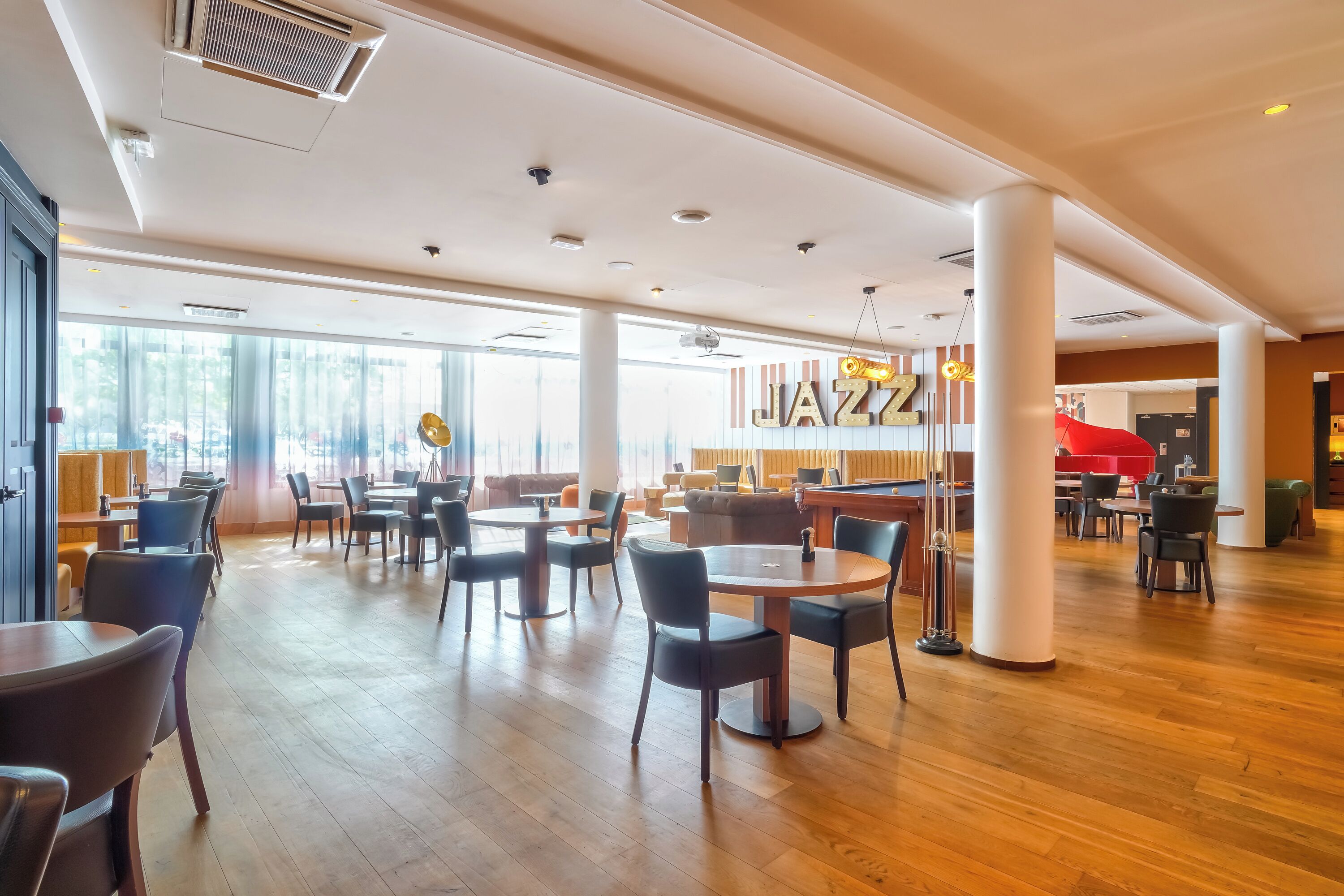 Un espace intérieur spacieux doté d’un plancher en bois, de plusieurs tables et chaises, ainsi que d’une grande fenêtre laissant entrer la lumière naturelle.