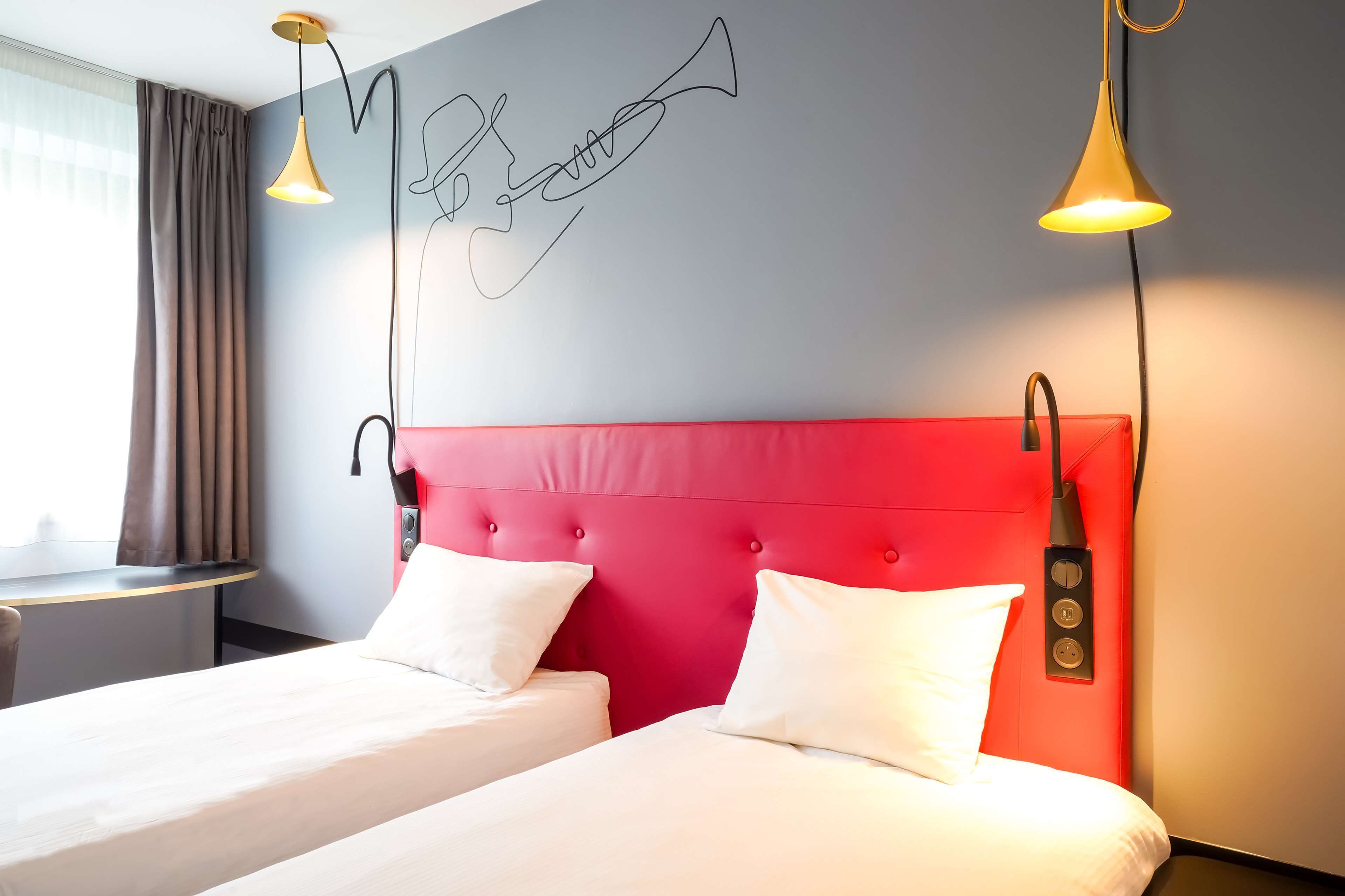 A hotel room with two beds, a red headboard, and a wall art of a trumpet.