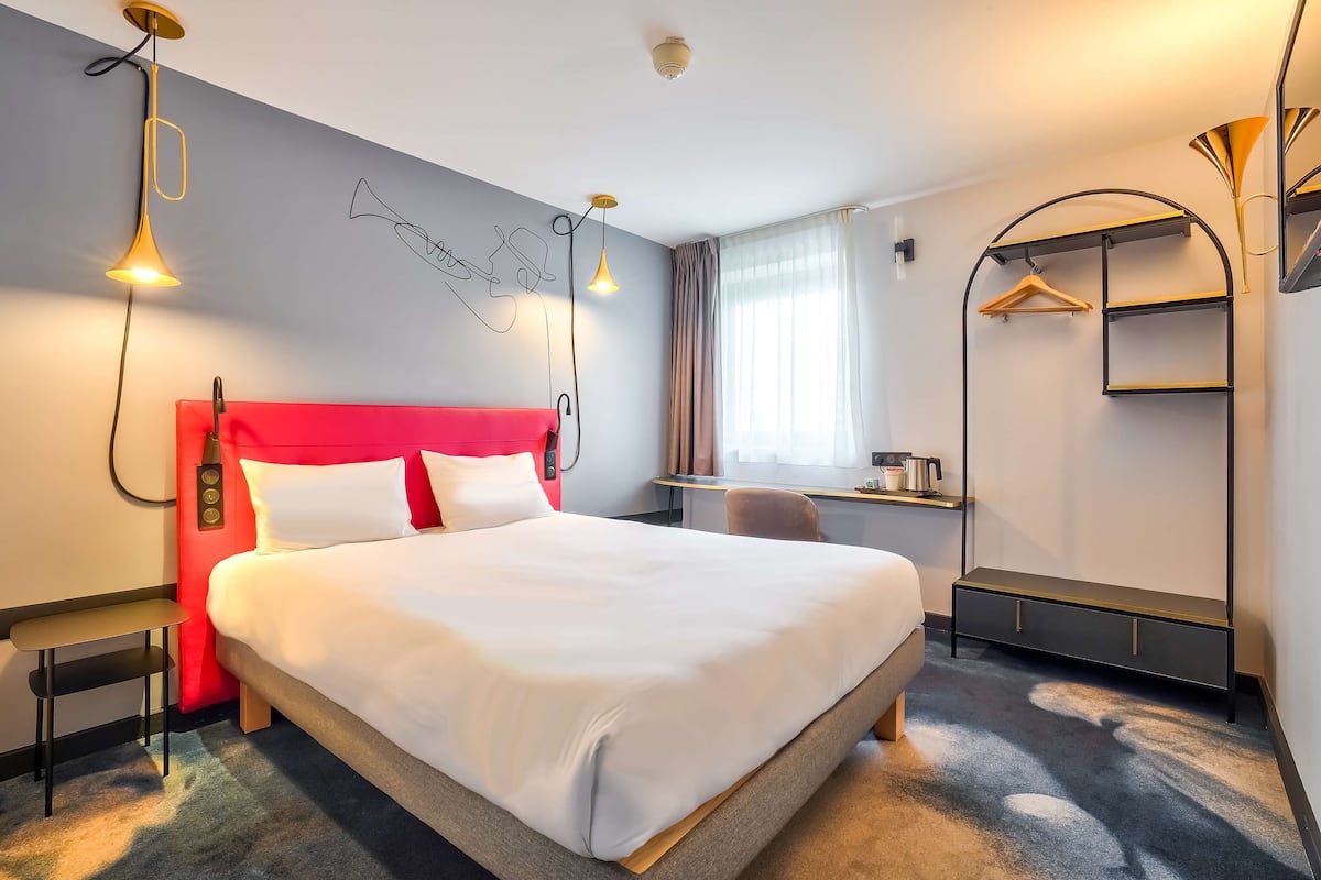 Hotellihuone, jossa on suuri sänky, työpöytä tuolilla, vaatekaappi ja naulakko.
