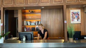 A reception desk with a wooden panel backdrop, a bookshelf with books and a 'JAZZ PORTRAITS' sign, and a framed collage on the wall. - Hotel Kyriad Créteil/Bonneuil-sur-Marne (Bonneuil-sur-Marne)