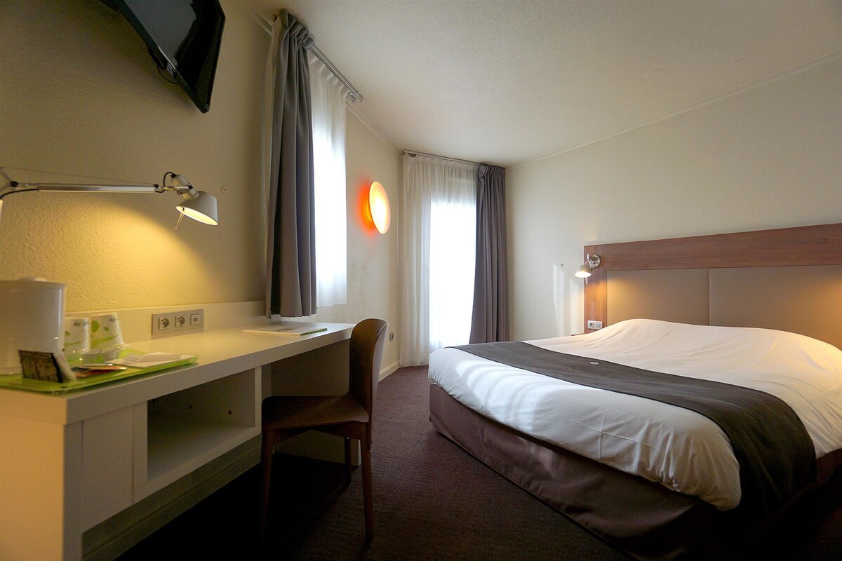 A hotel room with a bed, desk, chair, and a flat-screen TV mounted on the wall.