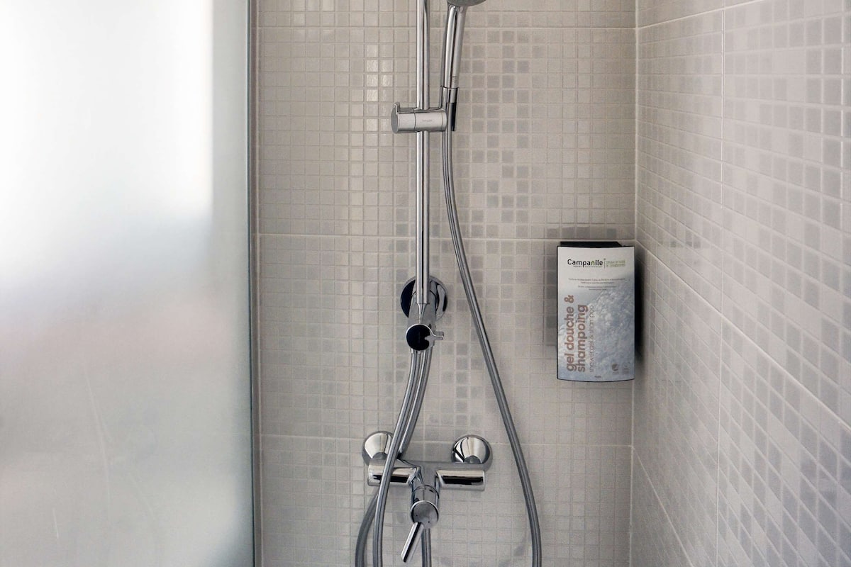 A modern shower with a handheld showerhead, a wall-mounted control panel, and a soap dispenser.