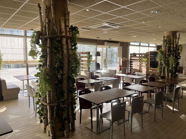 Un espacio interior moderno con mesas y sillas, ventanas amplias e instalaciones decorativas de plantas.