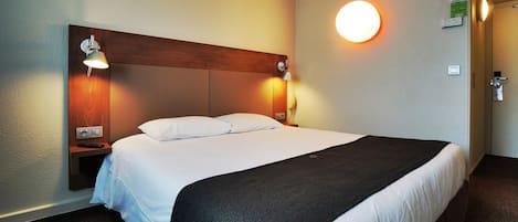 Habitación de hotel con una cama grande, dos lámparas de noche, una luz de pared redonda y un cabecero de madera.