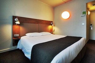Habitación de hotel con una cama grande, dos lámparas de noche, una luz de pared redonda y un cabecero de madera.