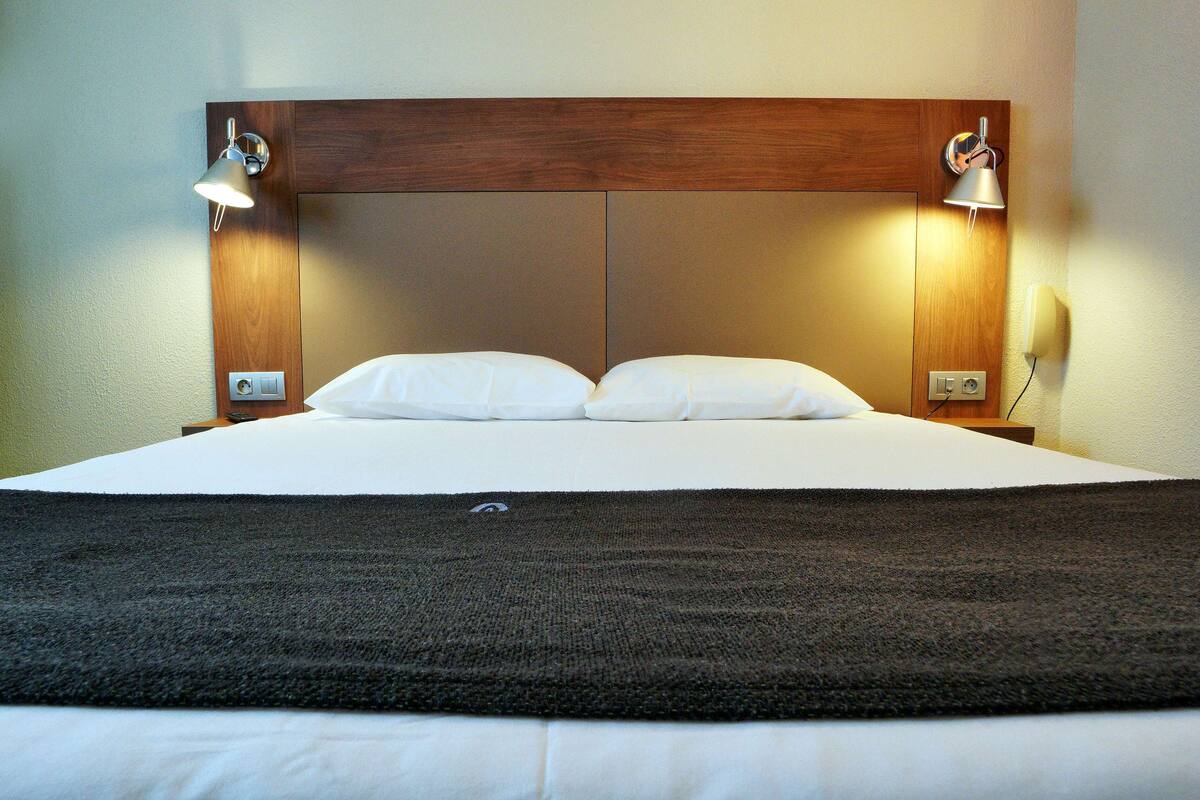 A hotel room with a large bed, two bedside lamps, and a wooden headboard.