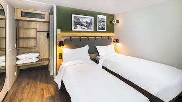 Ett hotellrum med två separata sängar, en garderob i trä, en bänk med handdukar och två inramade tavlor på väggen.