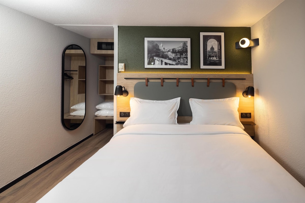 A neatly made bed with white linens, a headboard with a light fixture, and two framed pictures on the wall.