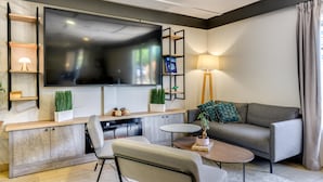 A modern living room with a flat-screen TV, a sofa, a coffee table, and a TV stand with shelves. - Campanile NATURE - Paris Ouest Gennevilliers Port (Gennevilliers)