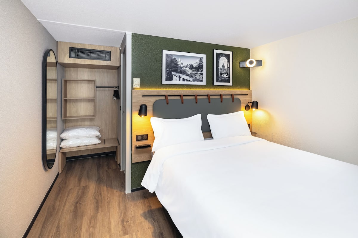 A hotel room with a bed, a built-in wardrobe, and a wall-mounted shelf.