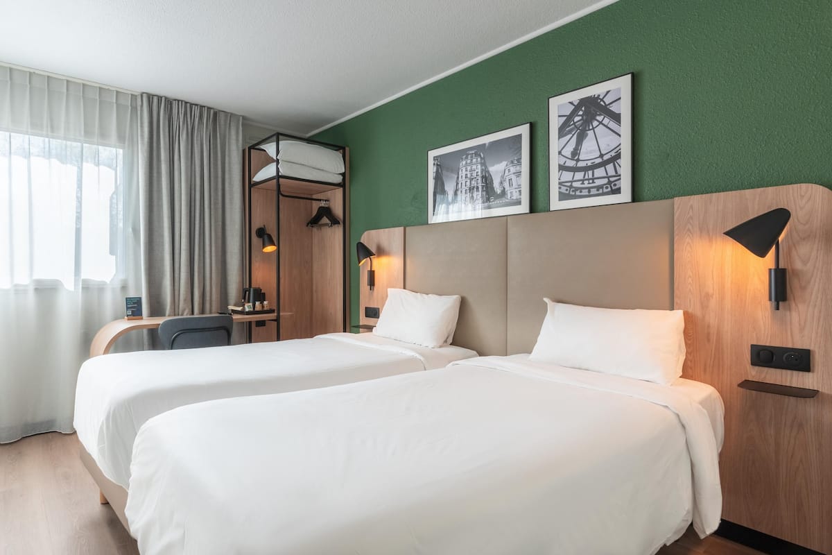 Une chambre d’hôtel avec deux lits, un bureau, une chaise et une fenêtre avec des rideaux.