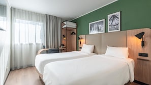 A hotel room with two beds, a desk, a chair, and a window with curtains.