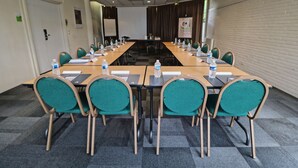 A conference room with a long table, green chairs, water bottles, and a projector screen. - Campanile PRIME - Paris Gennevilliers Barbanniers (Gennevilliers)