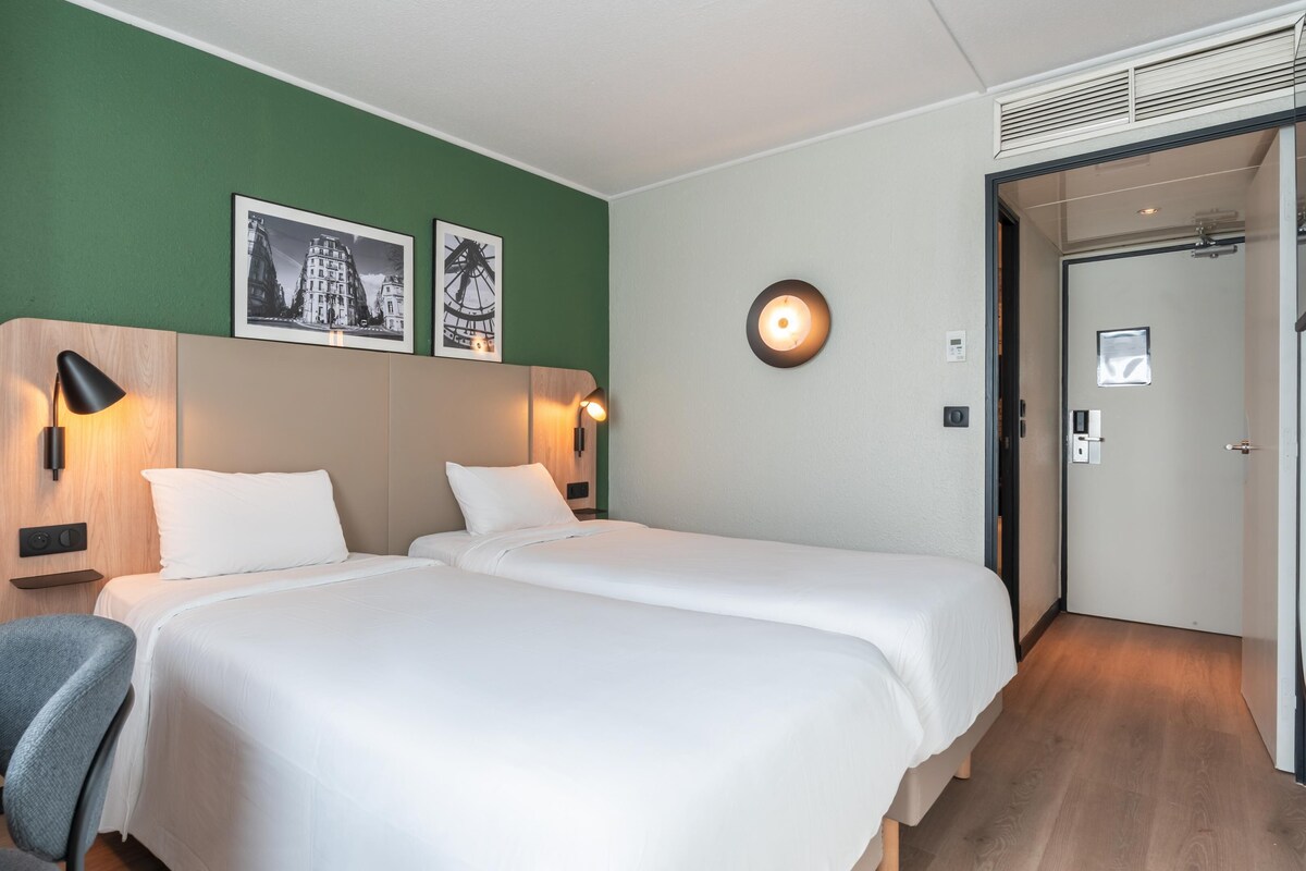 A hotel room with two beds, green walls, and a door leading to another room.