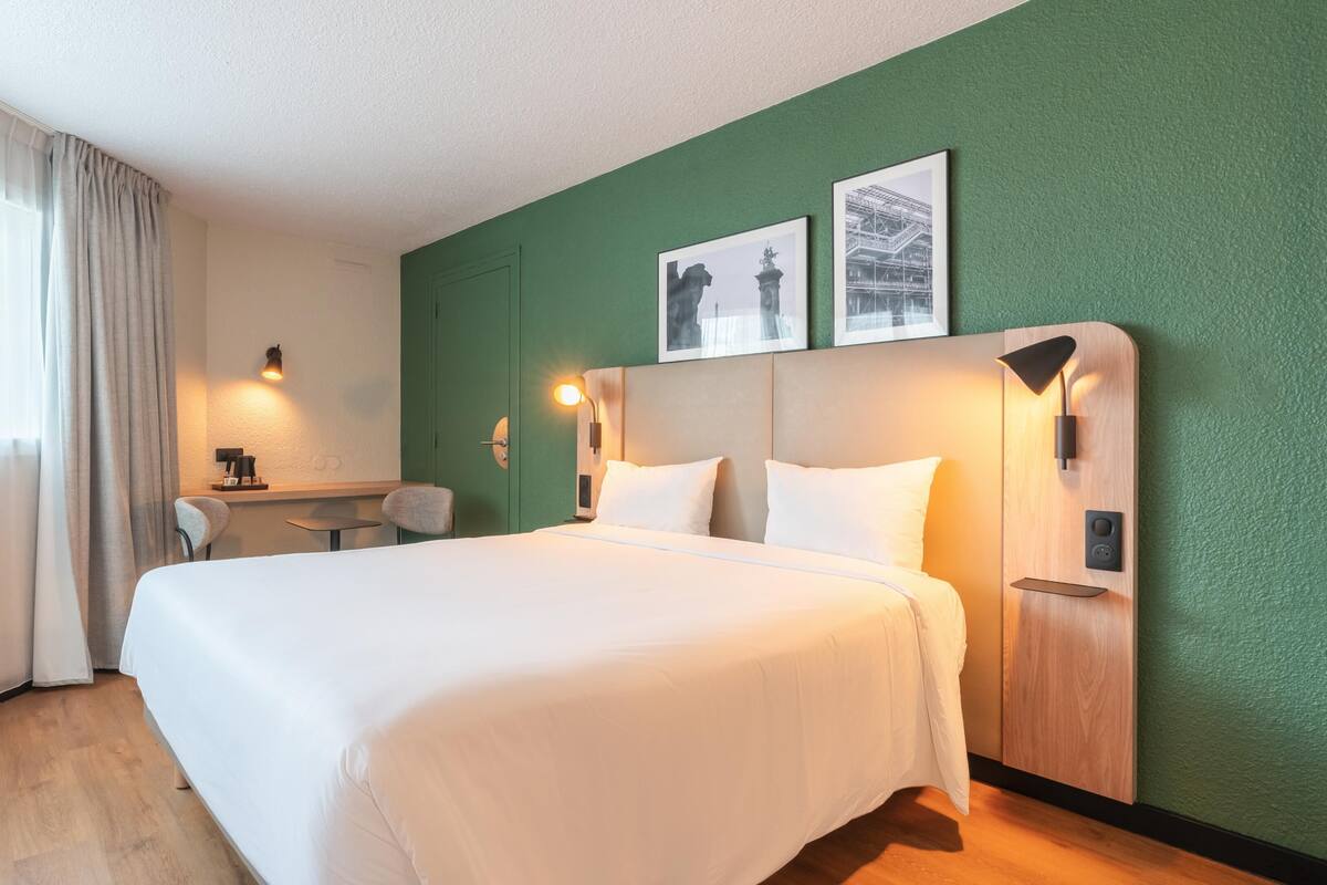 Une chambre d’hôtel équipée d’un lit, d’un bureau, d’une chaise et de deux lampes fixées au mur.