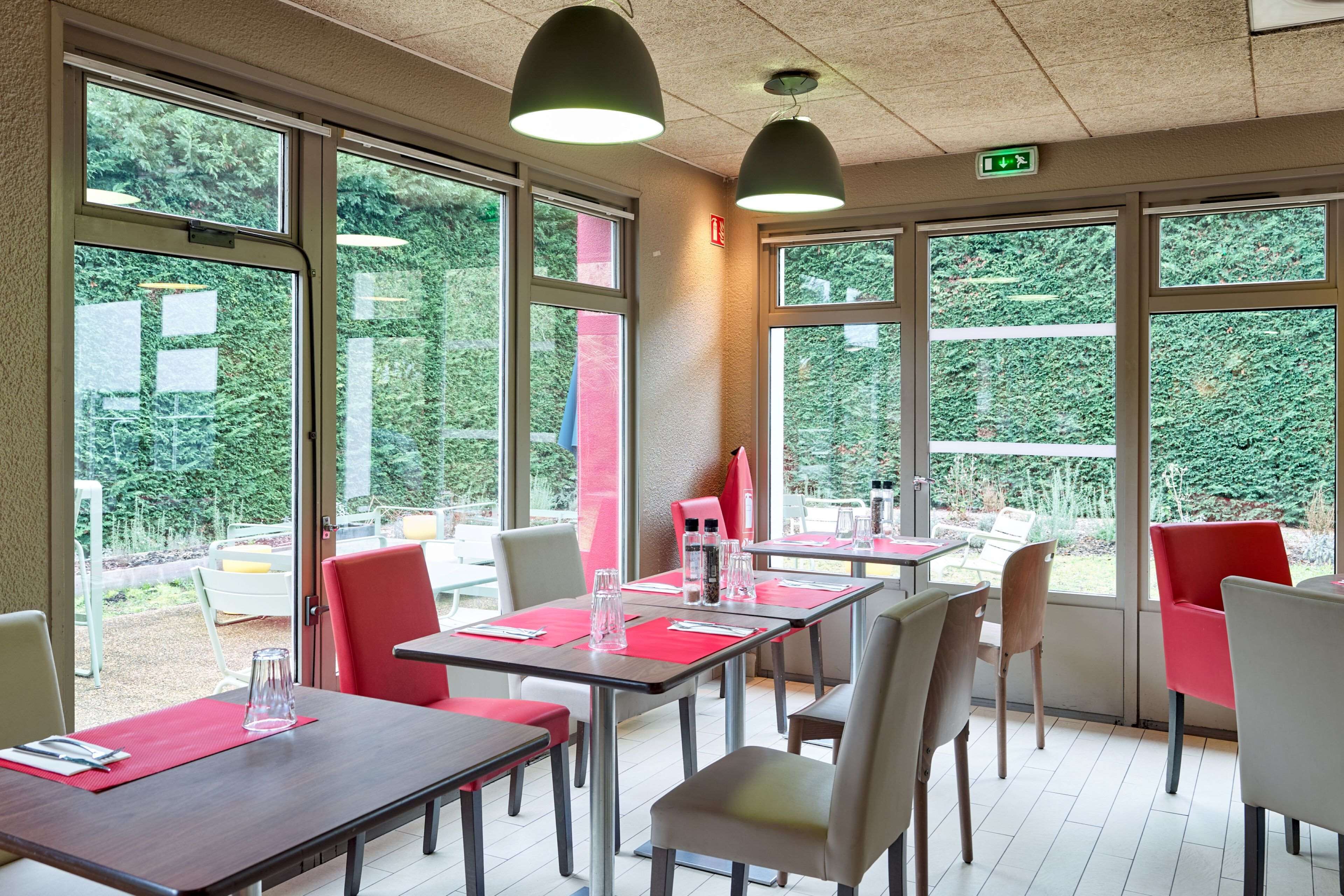 A restaurant with tables and chairs, large windows, and a view of greenery outside.