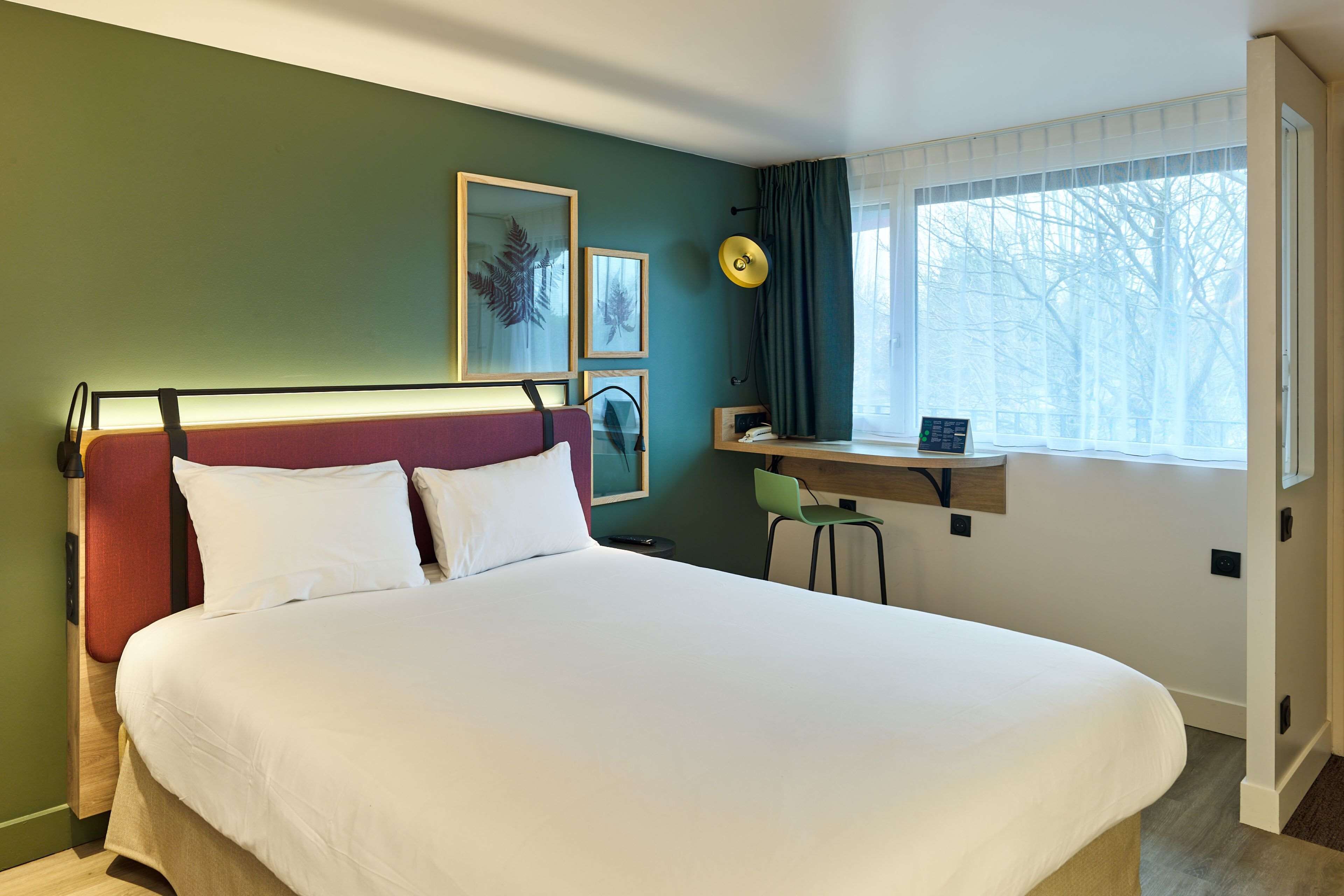 A neatly arranged hotel room with a bed, a desk, and a window with a view of trees.