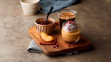 Une présentation de desserts comprenant un verre de café, un bol de chocolat et une part de gâteau, le tout disposé sur une planche en bois.